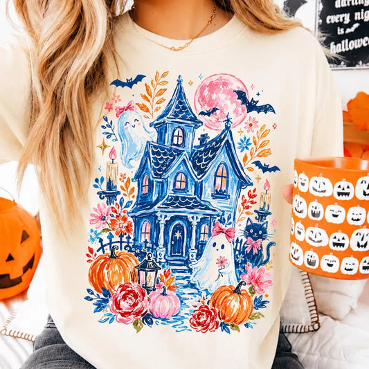 Vibrant Halloween DTF transfer design on a cream sweatshirt as seen in file Cute_ghost The graphic features an intricate blue sketch-style haunted house surrounded by orange and pink pumpkins, autumn flowers, bats, candles, a black cat with a pink bow, and two cute ghosts wearing pink coquette bows. Ready to press heat transfer.