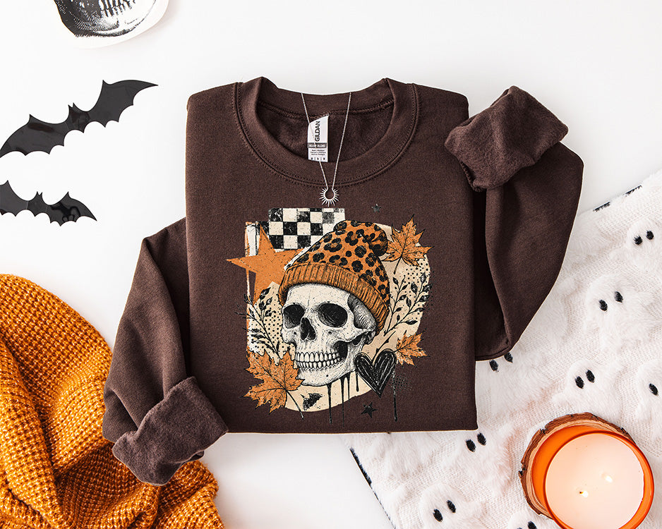 Edgy fall skull DTF transfer featuring a skeleton skull wearing an orange leopard print beanie with autumn leaves, checkerboard accents and black heart details