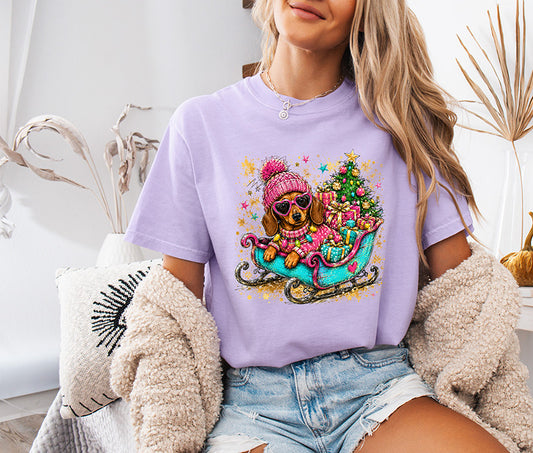 Colorful Christmas dachshund DTF transfer featuring a wiener dog in pink winter accessories riding a turquoise sleigh with Christmas tree and presents