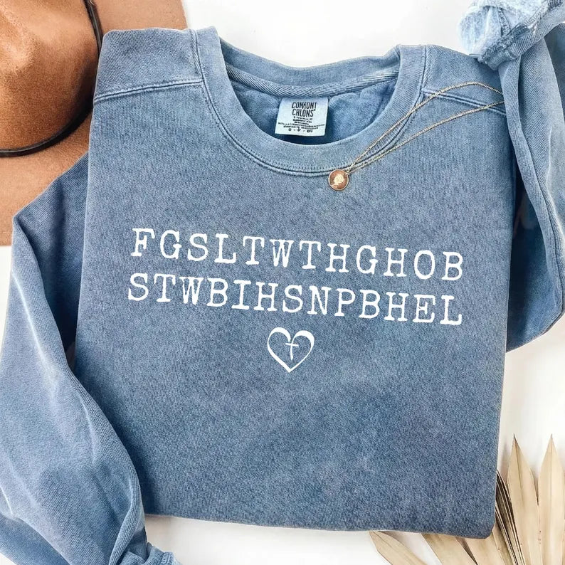 Ready to press white John 3:16 Bible verse acronym DTF transfer featuring the letters FGSLTWTHGHOB STWBIHSNPBHEL with a cross heart graphic, pressed onto a vintage blue mineral wash crewneck sweatshirt.