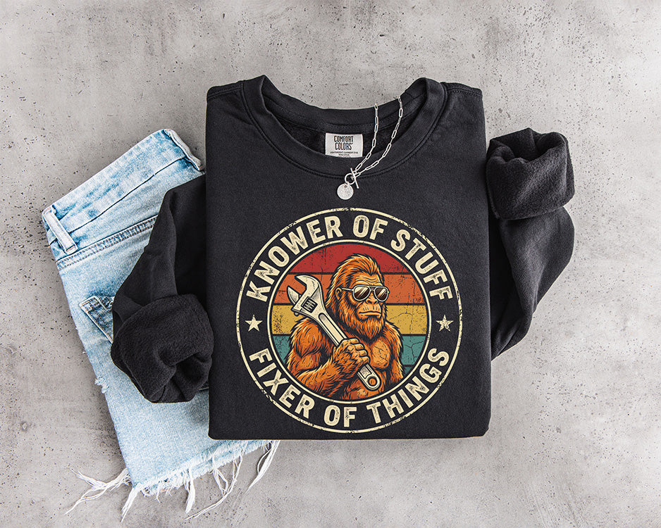 Knower of Stuff Fixer of Things DTF transfer featuring retro Bigfoot holding a wrench with vintage sunset background