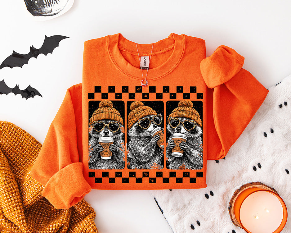 Pumpkin Spice Raccoon fall DTF transfer featuring three raccoons wearing orange beanies and heart sunglasses while drinking pumpkin spice coffee in a black checkerboard frame