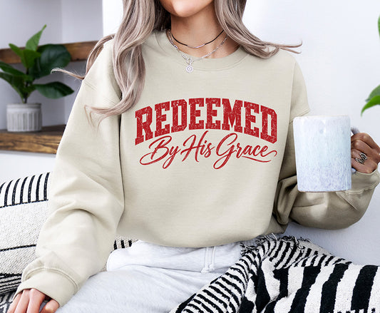 Redeemed By His Grace red distressed Christian DTF transfer displayed on a neutral sweatshirt