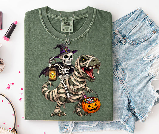 Halloween DTF transfer featuring witch skeleton riding a mummy wrapped T-Rex carrying a pumpkin candy bucket and glowing jack o lantern